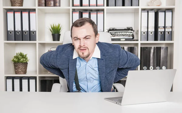 Knappe zakenman met pijn in zijn rug in zijn kantoor — Stockfoto