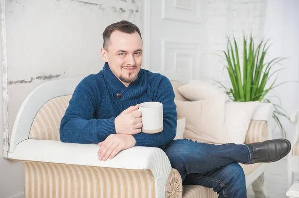 Bonito homem sorridente com xícara de café sentado no sofá em casa — Fotografia de Stock