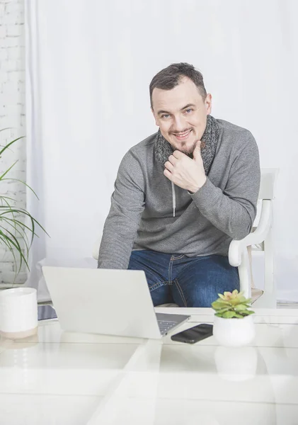 Красивий щасливий чоловік працює з ноутбуком зі смартфоном вдома — стокове фото