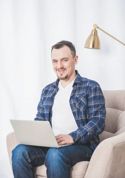 Красивый счастливый человек работает с ноутбуком на диване дома — стоковое фото