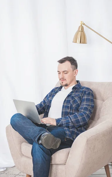 Красивий щасливий чоловік працює за допомогою ноутбука на дивані вдома — стокове фото