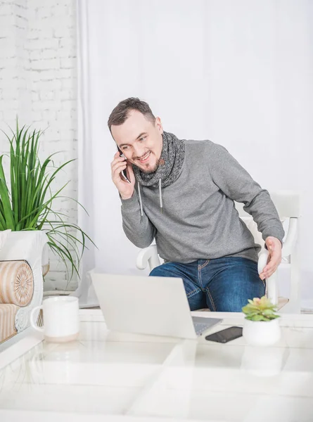 Усміхнений чоловік працює за допомогою ноутбука і розмовляє зі смартфоном на — стокове фото