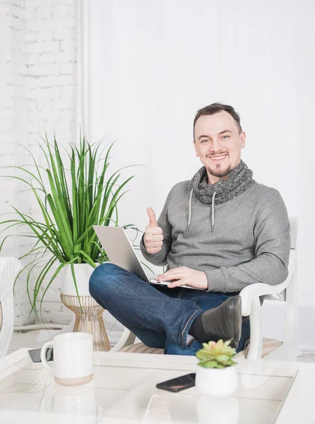 Красивый счастливый человек, работающий на ноутбуке, показывающий большие пальцы в доме — стоковое фото