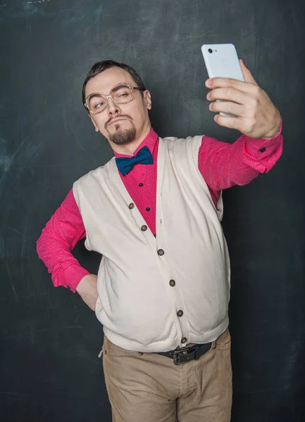 Portrait of funny nerd man making selfie on blackboard background