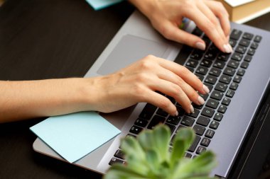 Siyah ofis masaüstüne yerleştirilmiş gümüş dizüstü bilgisayarda yazan kadın elleri.