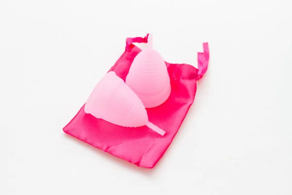 Две менструальные чашки многоразового использования на розовом мешке на белом фоне — стоковое фото