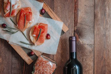 Jambonlu sandviçler, taze zeytinler ve tahta bir tahtanın üzerinde şarap şişesi.