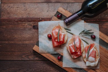 Ahşap tahtada jambonlu ve zeytinli sandviç. Şarap şişesi ve prosciutoo.