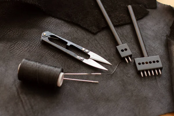 Set of leather work tools on black leather. Workplace for shoemaker.
