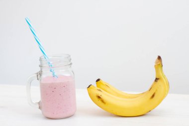 Beyaz arka planda taze pembe smoothie ve muzlu mavi pipet.