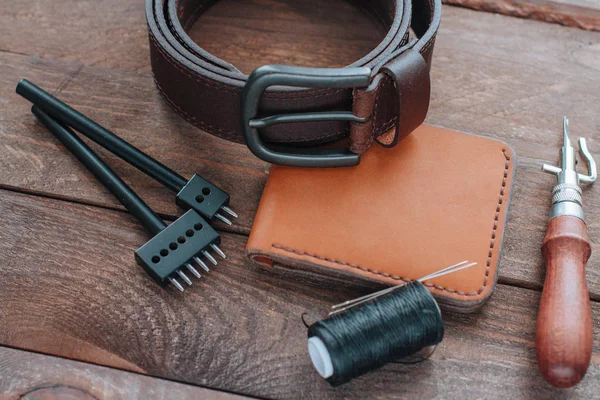 Brown leather belt, wallet and leather crafting tools on wooden desk