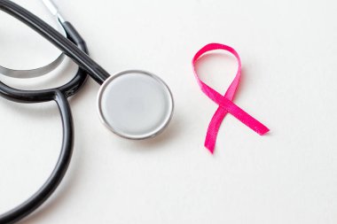 Göğüs kanseri farkındalığı. Beyaz arkaplanda steteskoplu pembe kurdele..