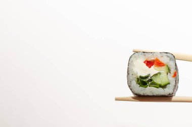 Beyaz arka planda yemek çubuklarında suşi rulosu tutuyor.