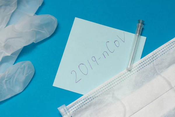 Nieuwe coronavirus ziekte genaamd 2019-ncov handschrift op blauw papier. Beschermend masker en chirurgische handschoenen — Stockfoto