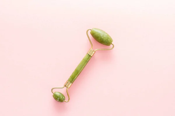 Green jade stone massager for face on a pink background — Stock Photo, Image