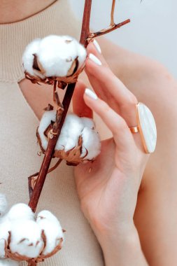 Pamuk dalı ve inci bir yüzüğü olan yumuşak bir kadın eli.