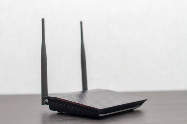 black wireless router with antennas on a black computer table on a gray background