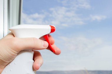 Pencere camını sprey deterjanla temizliyorum. Pencerede sprey ve mavi gökyüzü