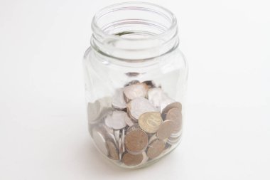 Beyaz arka planda cam bir kavanozda bozuk paralar olan kumbara..