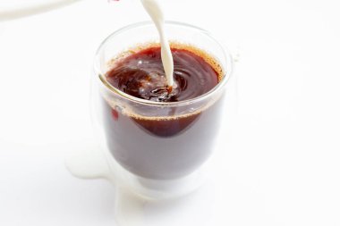 Masadaki mason kavanozunda soğuk kahveye süt dökülüyor.