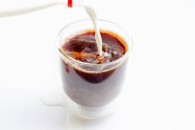 Beyaz arka planda demlenmiş kahveyle cam bardağa süt dökmek.