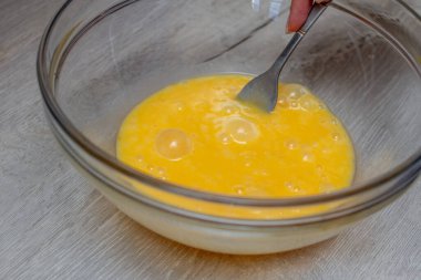 Kadının eli cam kasede yumurta çırpıyor.