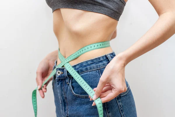 Thin young woman measuring her thin waist with a tape measure.