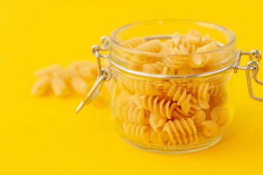 Sarı zemin üzerinde galss kavanozunda fusilli makarna yakın çekim.