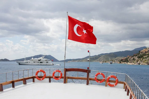 Drapeau de la Turquie sur un bateau en mer sur fond de montagnes et un yacht de luxe — Photo