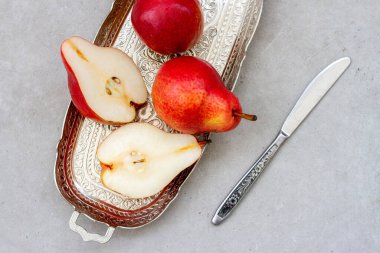 Gümüş tepside bir bıçakla olgun bir armut. Gri arka planda taze armut parçaları.