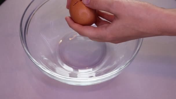 Een vrouw breekt een ei in een glazen schaal. Bereiding van ingrediënten voor het bakken. — Stockvideo
