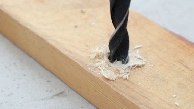 Elektrikli matkap ucu ahşap tahtada bir delik açıyor. Odun kesikleri metal matkaptan uçar.