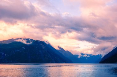 Norveç 'te fiyortta güzel bir günbatımı. Pembe bulutlu dağlar ve sudaki yansımaları.