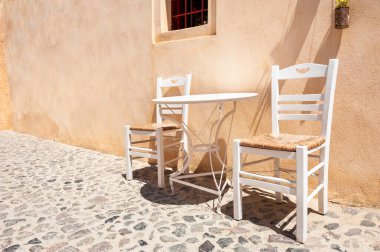 Sokakta masası olan iki beyaz tahta sandalye. Yunanistan 'ın Santorini adasında geleneksel Yunan mimarisi.