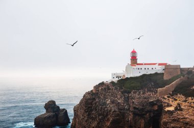Portekiz, Algarve 'de puslu bir akşamda St. Vincent Burnu' ndaki deniz feneri. Martılar gökyüzünde süzülüyor. Burası Avrupa 'nın en güneybatı noktası.
