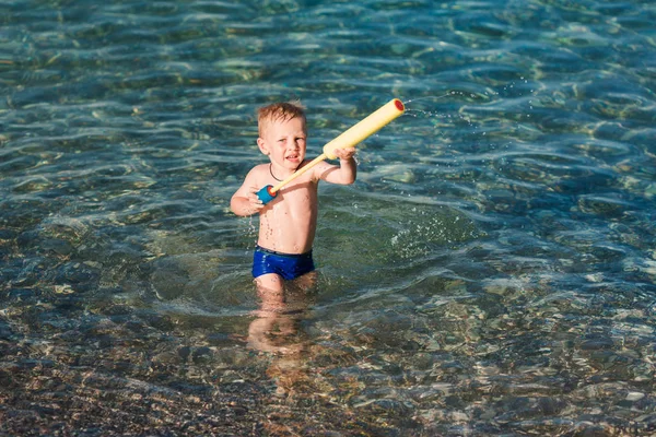 Miúdo feliz bonito brincando com pistola de água — Fotografia de Stock