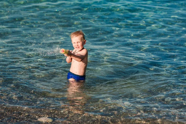 Miúdo feliz bonito brincando com pistola de água — Fotografia de Stock