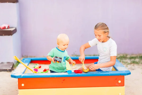Милий хлопчик грає зі своєю сестрою в пісочниці — стокове фото
