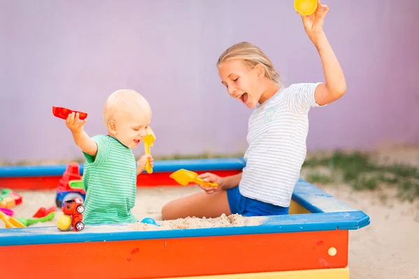 Милый мальчик играет со своей сестрой в песочнице — стоковое фото