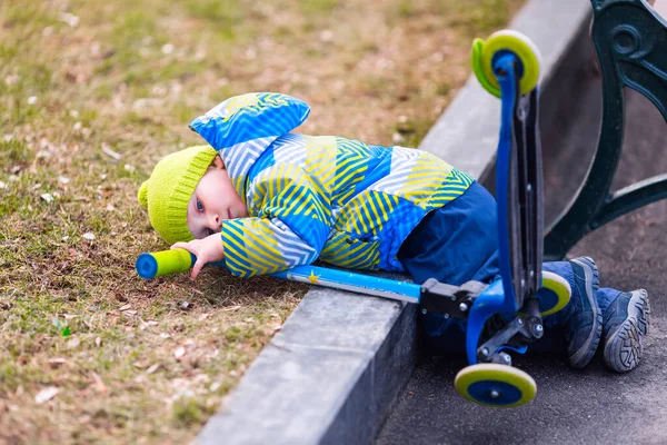 Cute little boy falling off his scooter . Kid getting hurt while riding a kick scooter. Falling scooter accident. Boy trying to stand up