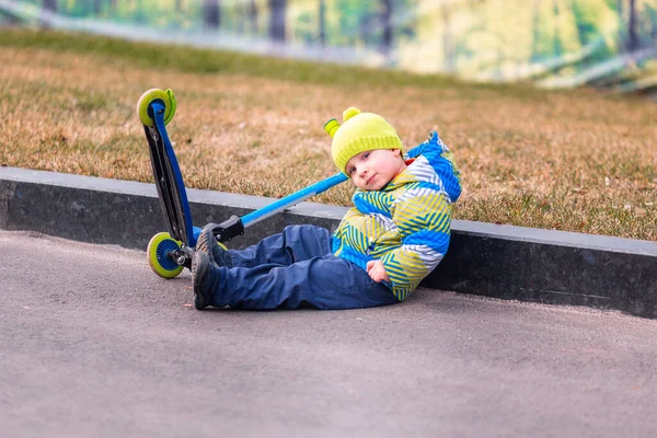 Cute little boy falling off his scooter . Kid getting hurt while riding a kick scooter. Falling scooter accident. Boy trying to stand up