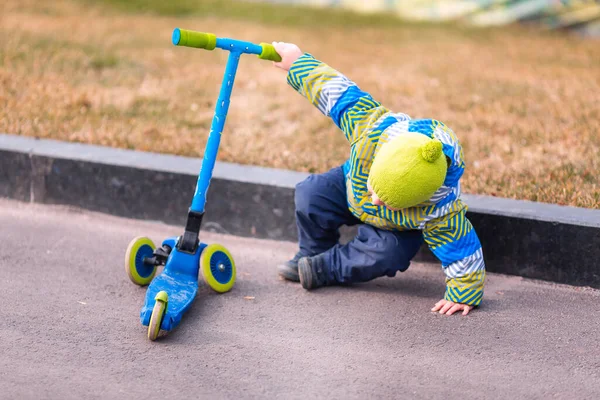 かわいい男の子はスクーターから落ちた キックスクーターに乗っている間に子供が怪我をします 落下スクーター事故 立ち上がろうとする少年 — ストック写真