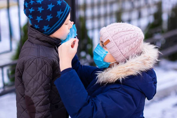若い女性は 隔離中に屋外の通りにコロナウイルスから保護するために小さな男の子にマスクを置くのを助ける医療面マスクを着ています コロナウイルス Covid パンデミック対策コンセプト — ストック写真