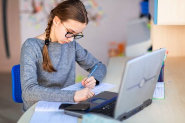 Güzel, genç bir kız solak, evinde bilgisayar ve ders notlarıyla çalışıyor. Sanal bir sınıfta. Karantina sırasında uzaktan eğitim ve öğrenme, e-öğrenme, çevrimiçi öğrenme kavramı