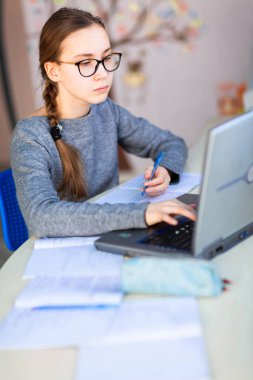 Güzel, genç bir kız solak, evinde bilgisayar ve ders notlarıyla çalışıyor. Sanal bir sınıfta. Karantina sırasında uzaktan eğitim ve öğrenme, e-öğrenme, çevrimiçi öğrenme kavramı