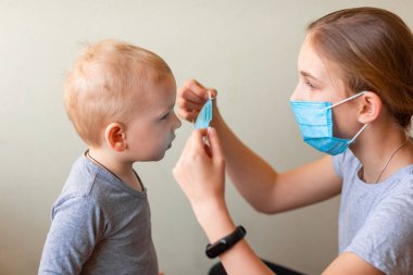 Genç kız kardeşinin tıbbi maske takmasına yardım ediyor. Coronavirus koruması, maske takmak.