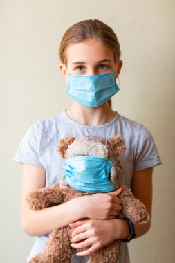 Oyuncak ayılı küçük bir kız. Maskeli, üzgün ve korkmuş. Coronavirus koruması, maske takmak.