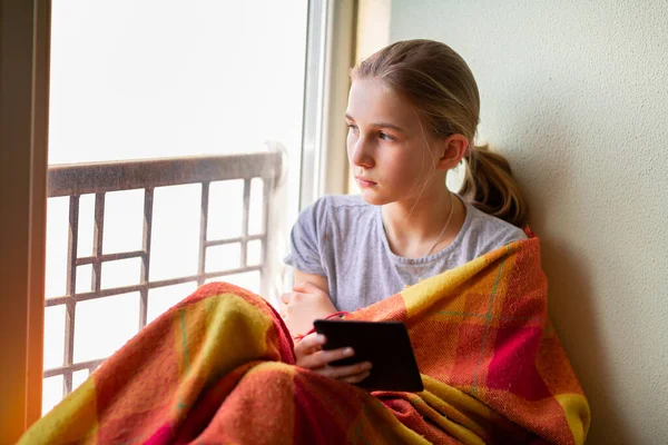 悲しい小さな女の子は 電子書籍やタブレットを読んで 家庭で孤立して勉強してウィンドウ上に座っている コロナウイルス隔離距離教育の概念 — ストック写真