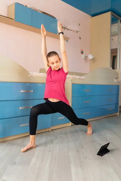 テニスの女の子は家でフィットネス体操をしています 体操ビデオチュートリアル 体操の練習 コロナウイルスのパンデミックの概念の間の隔離における子供の活動 — ストック写真