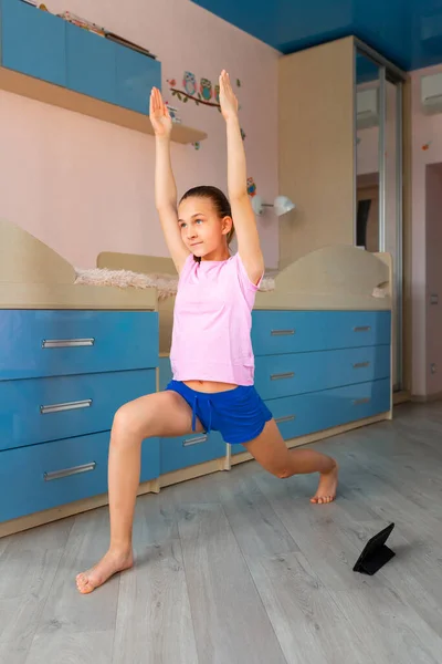 テニスの女の子は家でフィットネス体操をしています 体操ビデオチュートリアル 体操の練習 コロナウイルスのパンデミックの概念の間の隔離における子供の活動 — ストック写真